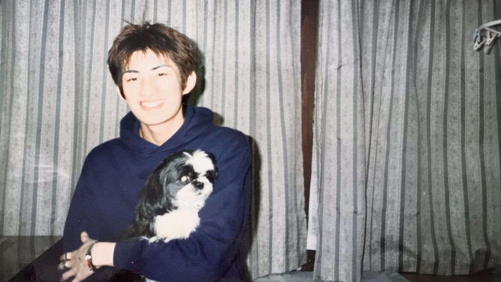 若い頃の男性が、白黒のシーズー犬を抱いて笑顔で写っている写真