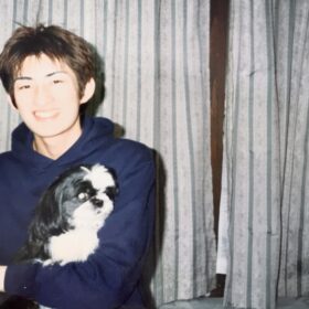 若い頃の男性が、白黒のシーズー犬を抱いて笑顔で写っている写真