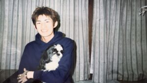 若い頃の男性が、白黒のシーズー犬を抱いて笑顔で写っている写真