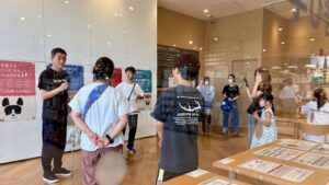 無印良品店内で開催された「これから犬を飼う人の相談会」で、講師が参加者に説明している様子。壁には犬に関するポスターが掲示されている。