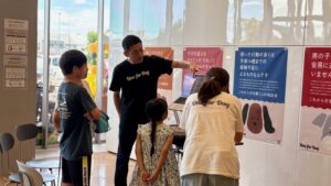 無印良品店内で講師がパソコンを使って犬の飼い方について説明している場面。壁には飼育に関する教育ポスターが並ぶ。