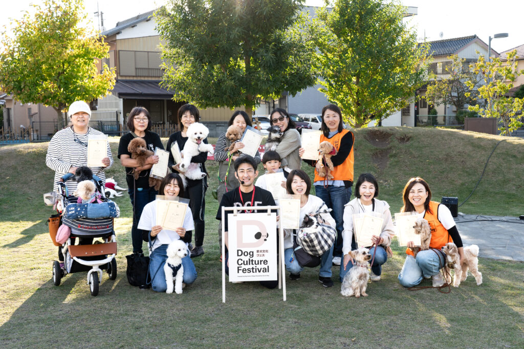 「Dog Culture Festival」の看板を囲み、修了証を手にした飼い主と愛犬たちが集合写真に収まっている。皆が笑顔でカメラに向かってポーズ。