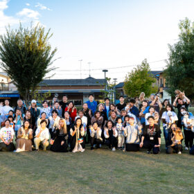 夕方の芝生広場で、愛犬と飼い主、スタッフが一堂に集まった大集合写真。笑顔でピースサインをする人や犬を抱く人など、フェスの締めくくりを飾る記念撮影の様子。