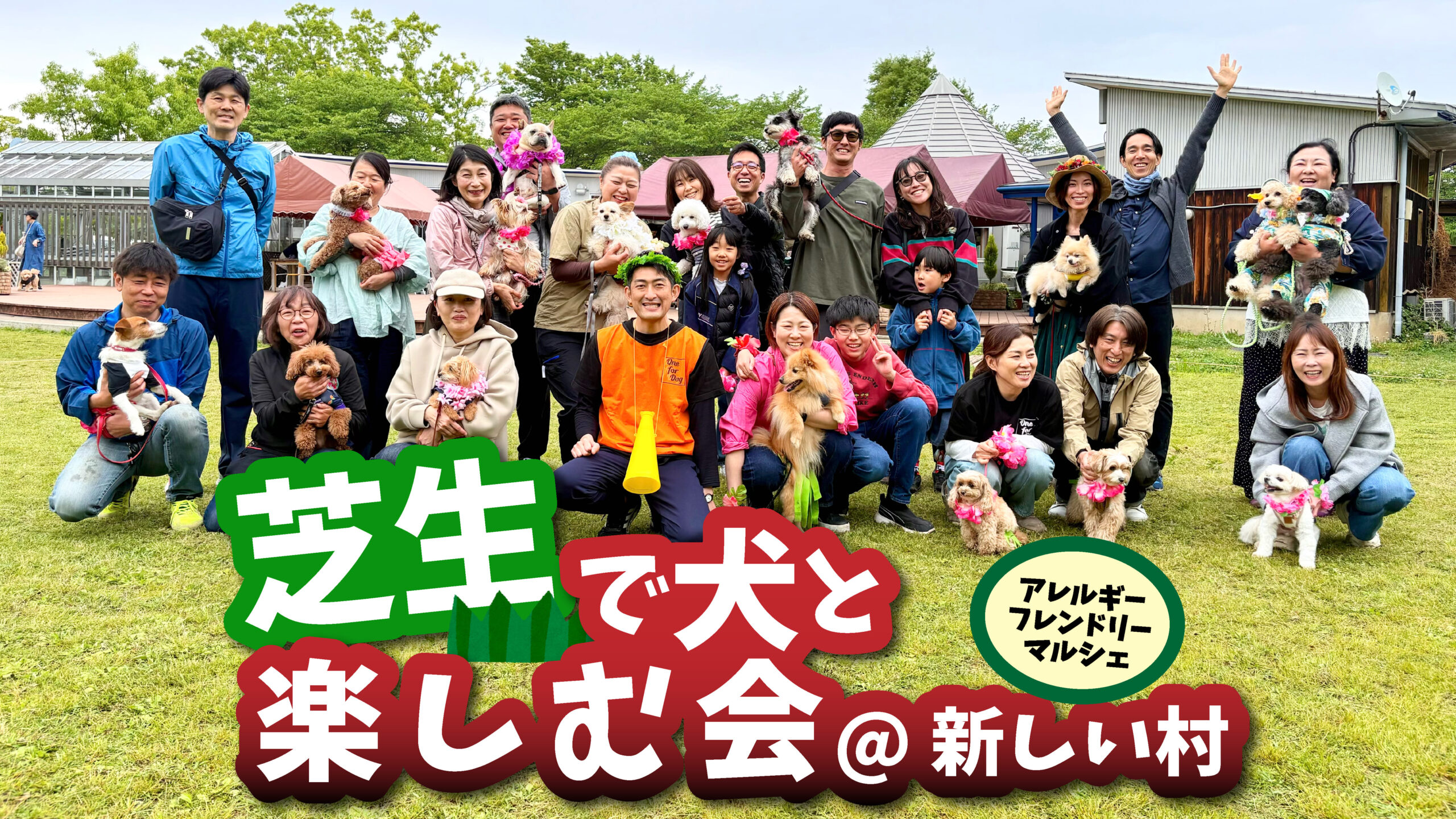芝生の広場で開催されたドッグイベントの集合写真。多くの飼い主と愛犬たちが並び、笑顔でカメラに向かっている。中央にはスタッフらしき人物が座り、周囲には小型犬を中心に抱っこされた犬やリード付きの犬が参加。背景にはテントや建物があり、屋外マルシェの雰囲気が感じられる。テキストで「芝生で犬と楽しむ会＠新しい村」「アレルギーフレンドリーマルシェ」と表示されている。