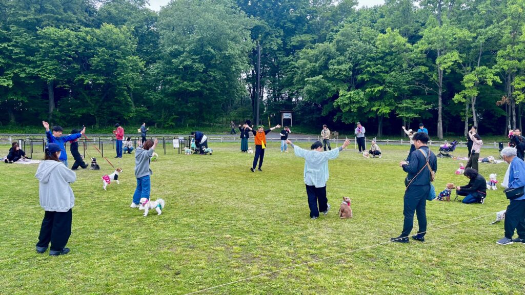 新しい村ドッグイベントで参加者と愛犬が芝生広場に円になりゲームを楽しむ様子